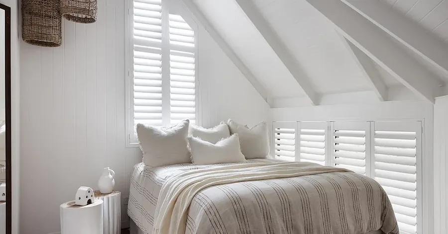 Plantation shutters in a bedroom beneath a pitched white ceiling